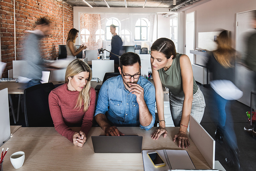 Business colleagues cooperating while working on laptop at corporate office. Their colleagues are walking in blurred motion.